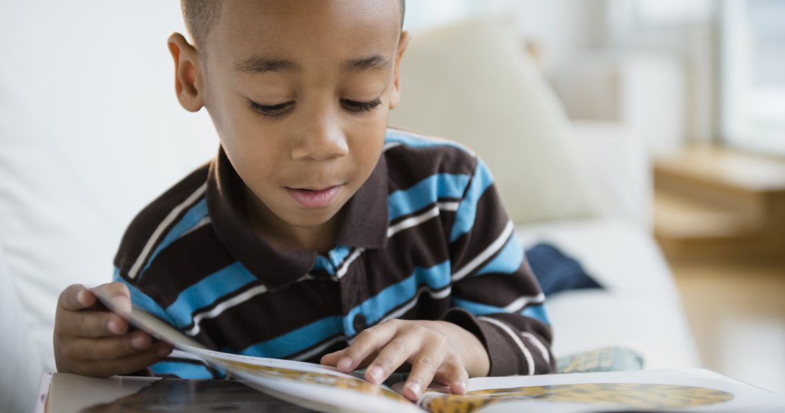African American boy reading book on sofa